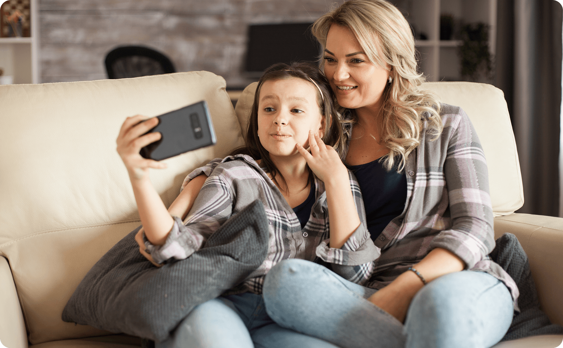 Mother and daughter sitting on couch taking a selfie together, representing our culturally responsive approach to mental health